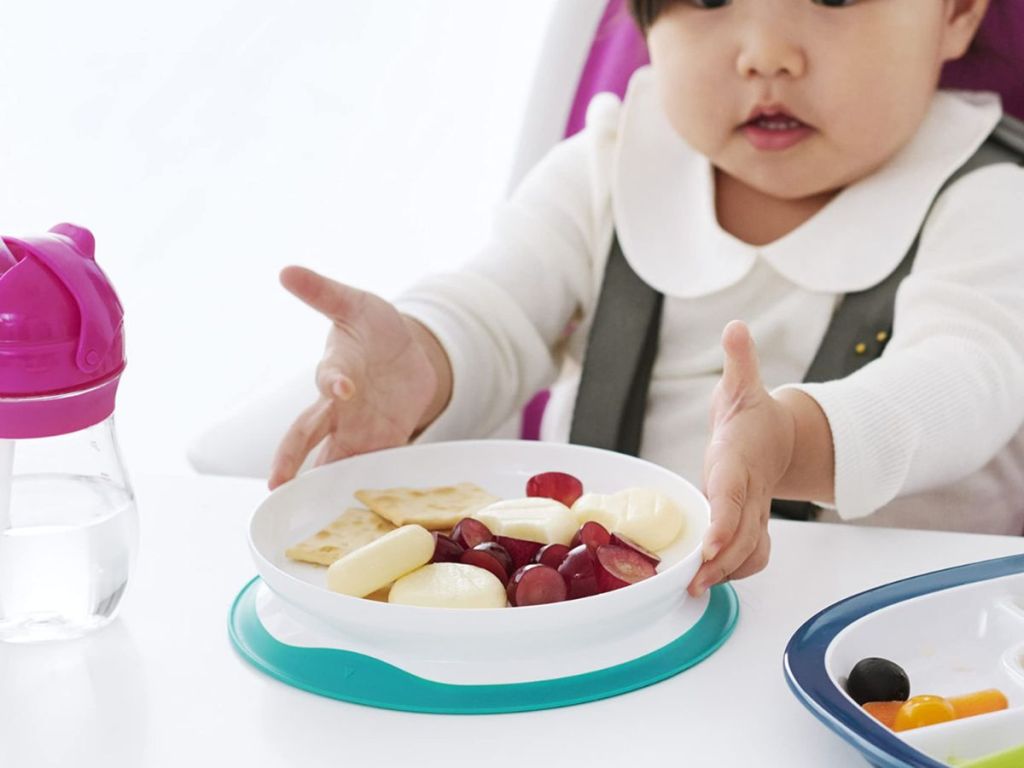 A toddler eating at a table with a plate of food