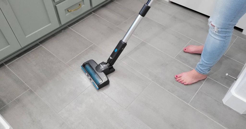 woman using stick vacuum on kitchen vinyl floor