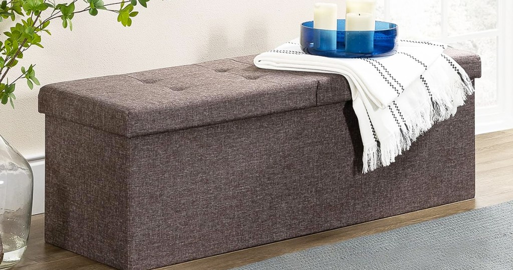 fabric storage ottoman with throw blanket and tray of candles on top