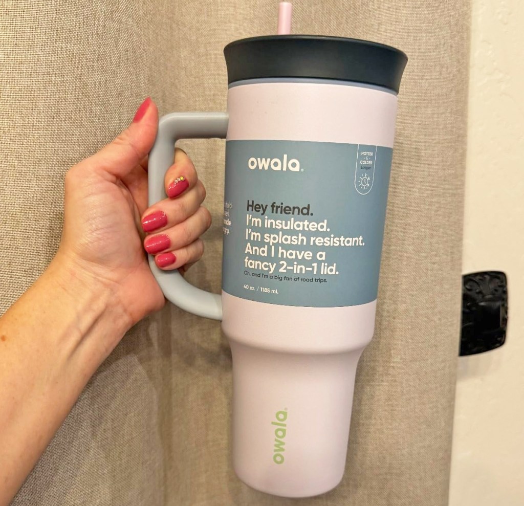 woman holding up a light pink owala tumbler with black lid