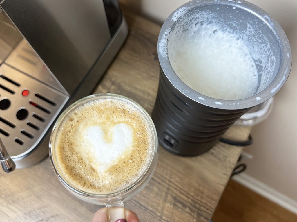 latte with foam heart next to a milk frother