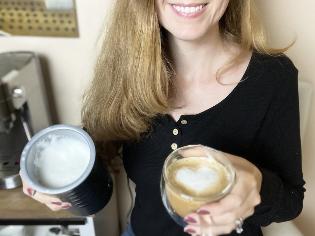 woman holding a milk frother and a latte with a foam heart