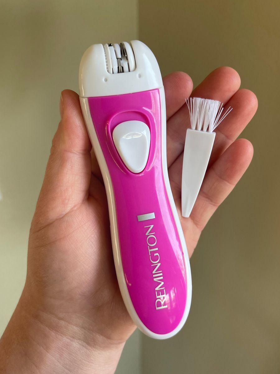 A pink epilator with a small brush being held in one hand