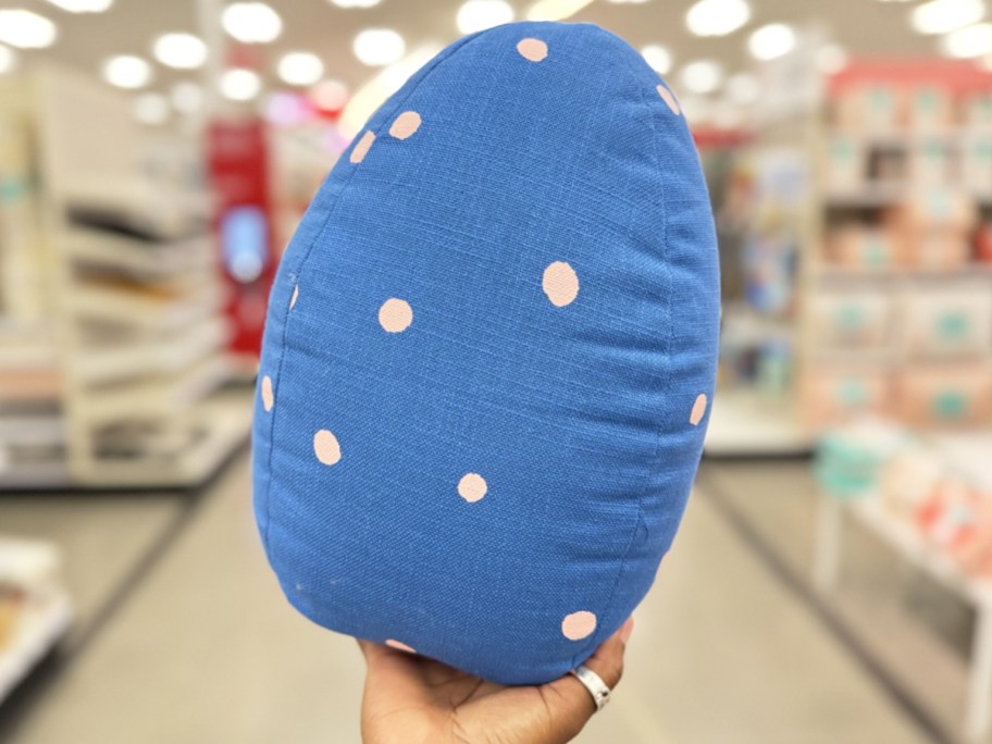 hand holding up a blue easter egg shaped throw pillow with pink polka dots