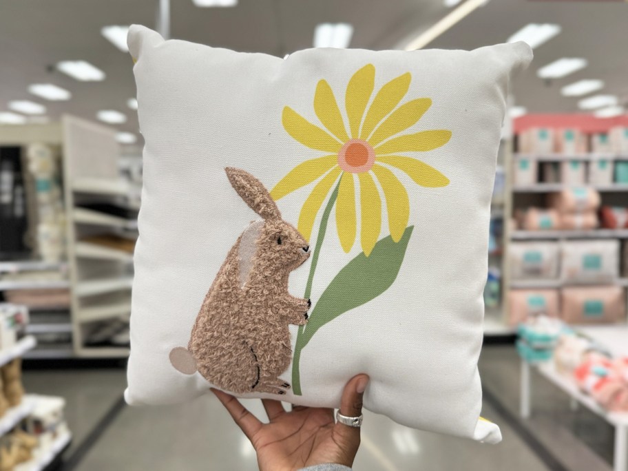 hand holding up a white throw pillow with a brown bunny and yellow flower
