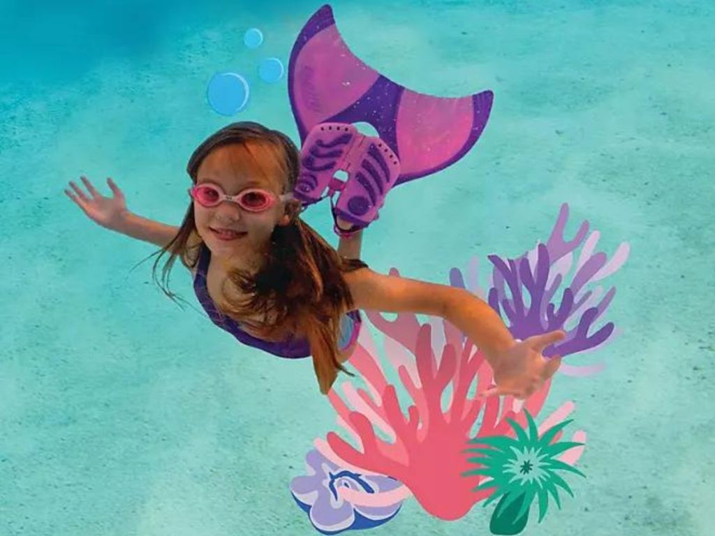 Little girl wearing swim goggles and a mermaid tail under water