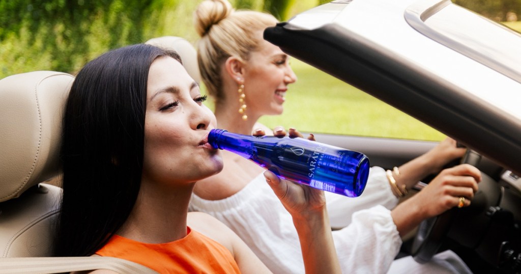 woman in car drinking from blue bottle of Saratoga Sparkling Spring Water