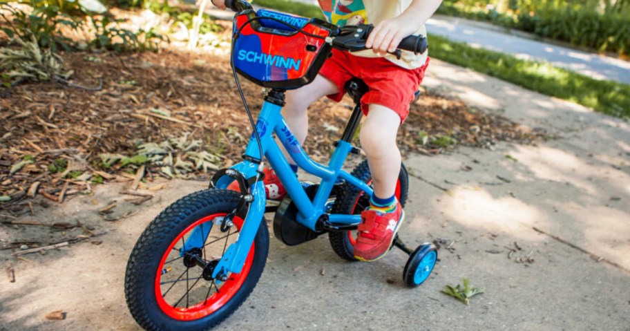 boy riding on a blue and red schwinn bike on sidewalk