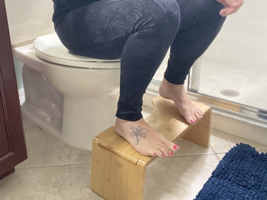 woman sitting on toilet with feet on bamboo squatty potty