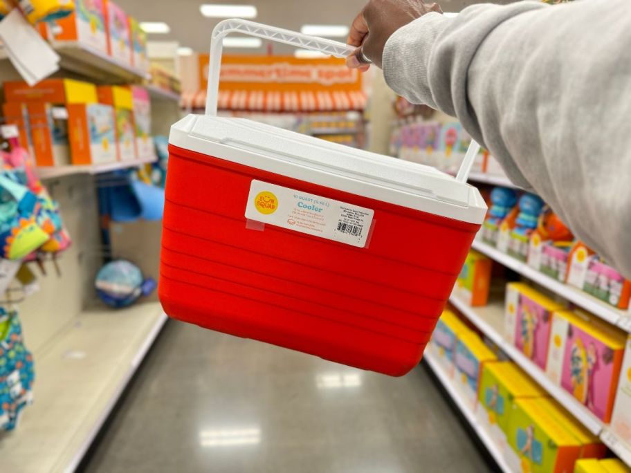 A hand holding a Sun Squad Hardside Cooler in red