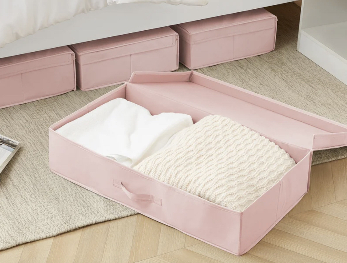 pink storage bin on floor with white clothes and blankets