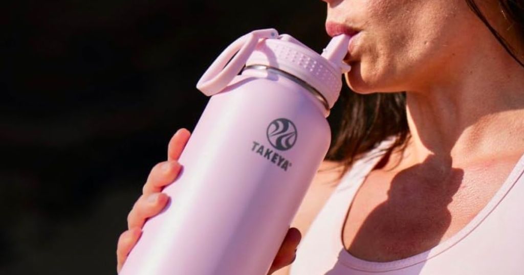 a woman drinking from a Takeya water bottle with a straw lid