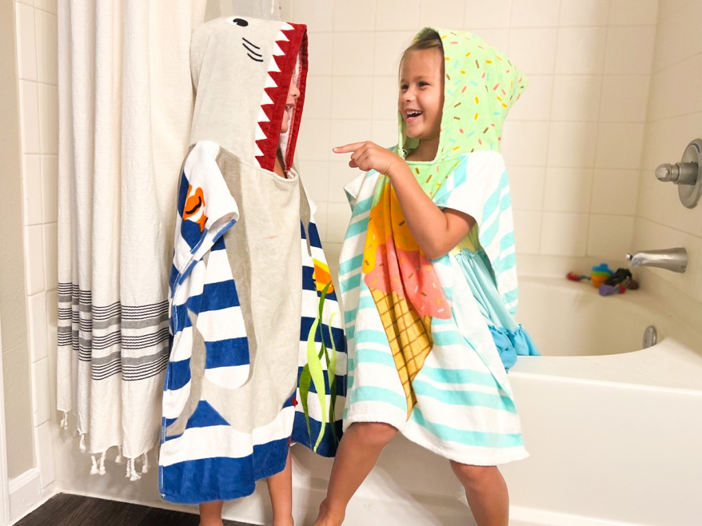 two kids sitting on side of bathtub in hooded towels