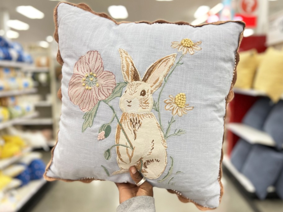 hand holding up a light blue throw pillow with a bunny and pink flower