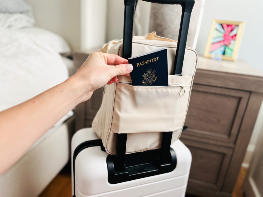 woman's hand pulling a passport out of her shoe organizer bag that is placed on top of her luggage