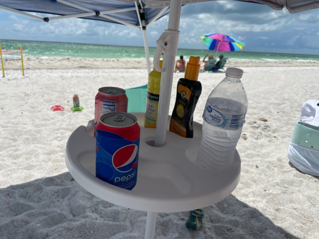 An umbrella table tray with drinks and sunscreen