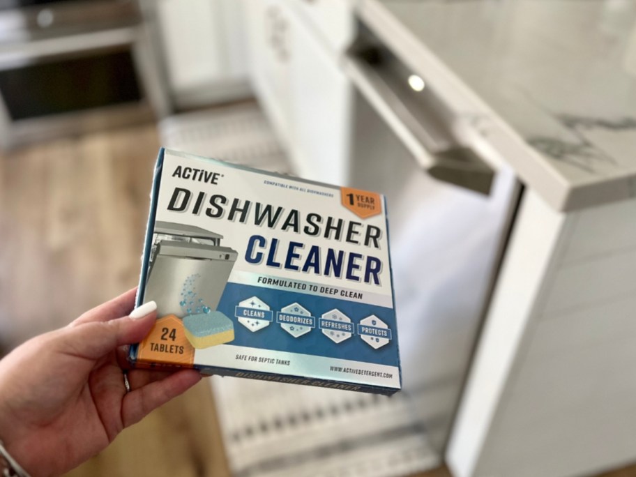 hand holding a box of Active Dishwashing Cleaner tablets in front of a dishwasher