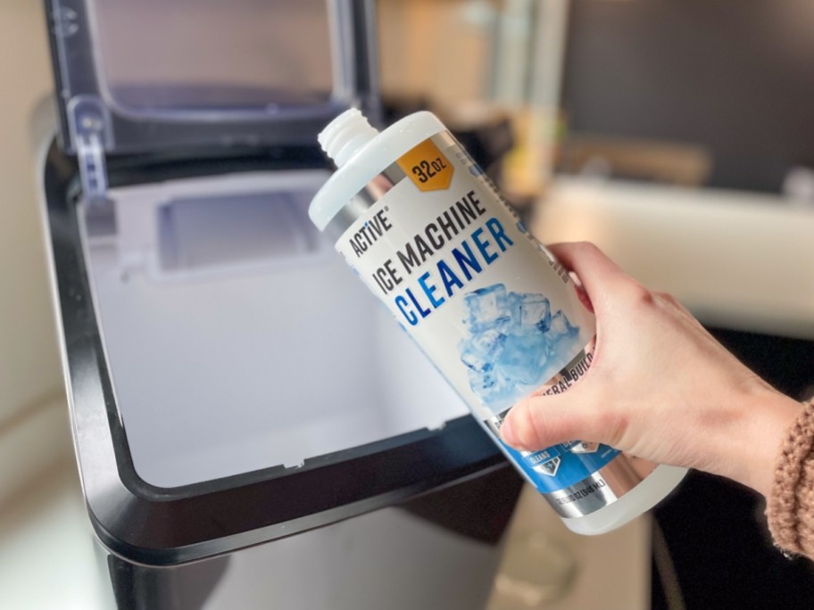 hand holding an open bottle of Active Ice Machine Cleaner in front of an ice machine