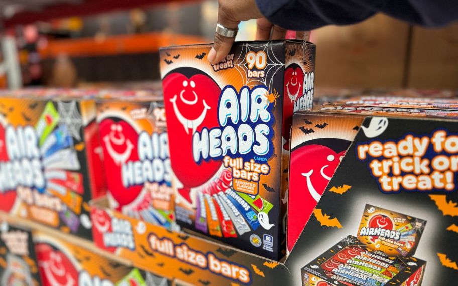 a womans hand grabbing a 90 count box of airheads from a store shelf