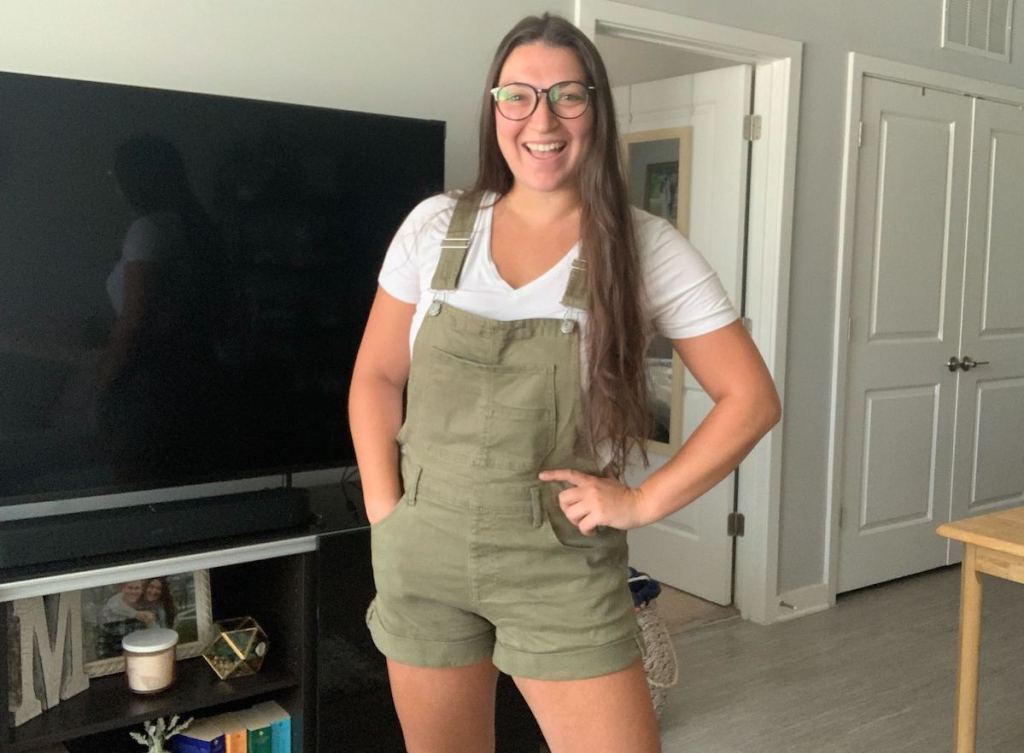 woman wearing green overalls and glasses posing in front of tv