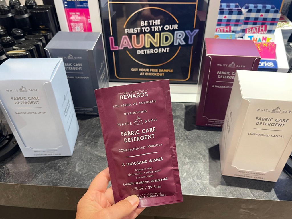 hand holding laundry detergent sample in front of signage