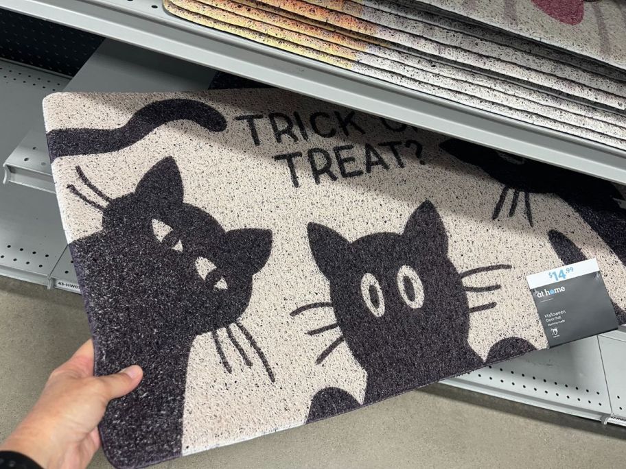 a womans hand grabbing a black cat door mat