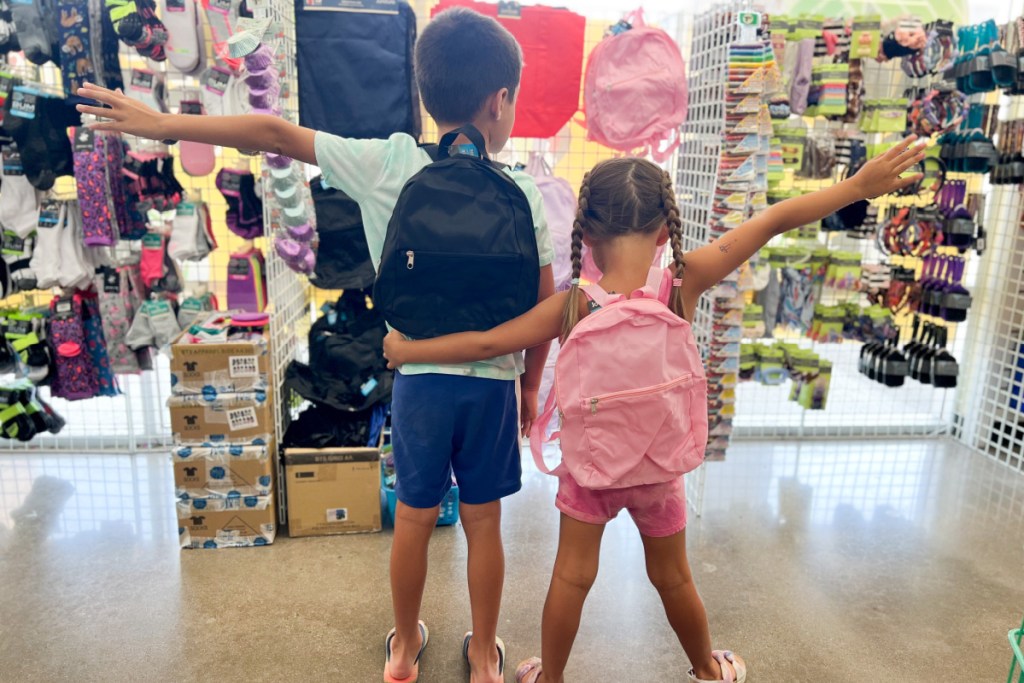 two kids standing in dollar tree wearing backpacks