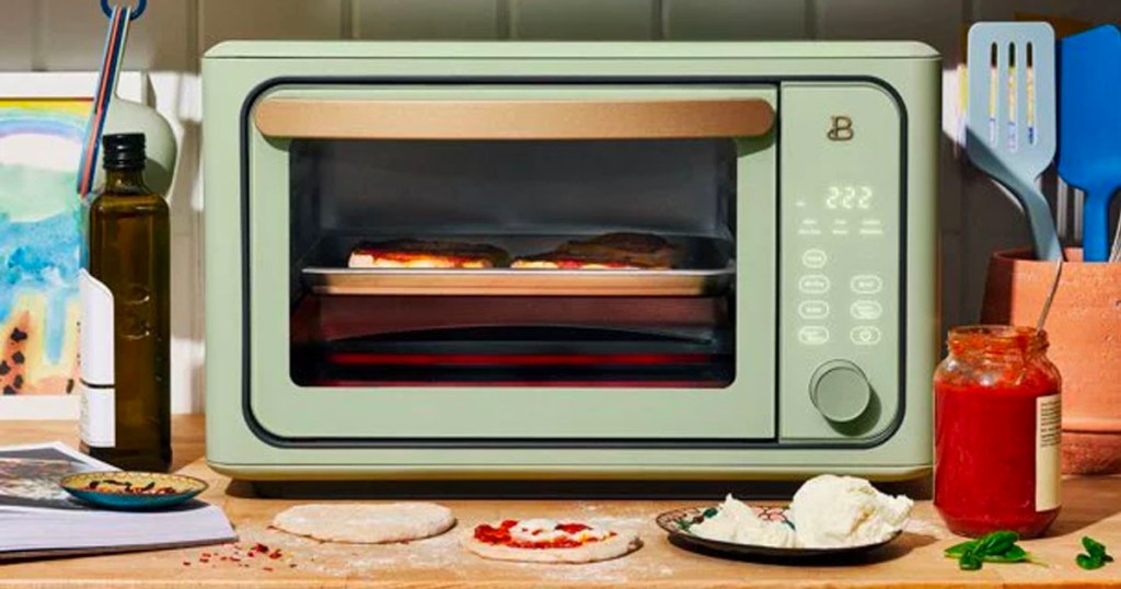 green drew barrymore toaster oven and air fryer on counter with pizza