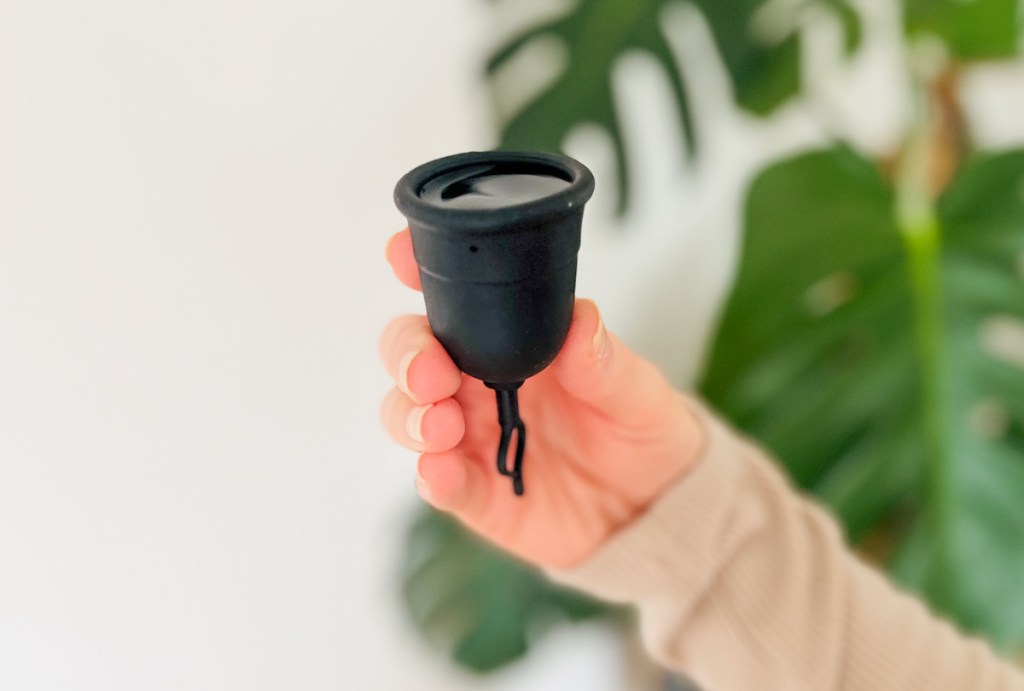 Hand holding a black menstrual cup filled with water