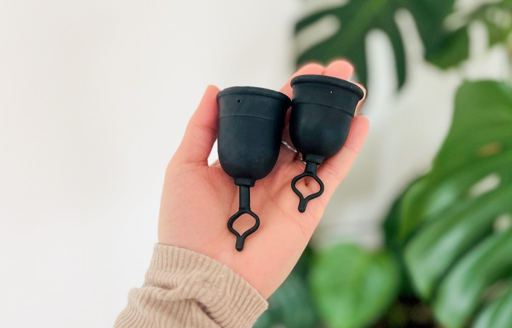 Hand holding two different sized black menstrual cups 