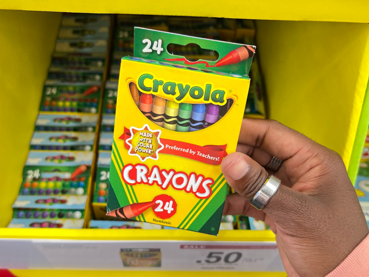 hand holding Crayola Crayons, 24-Pack at the store in front of its display