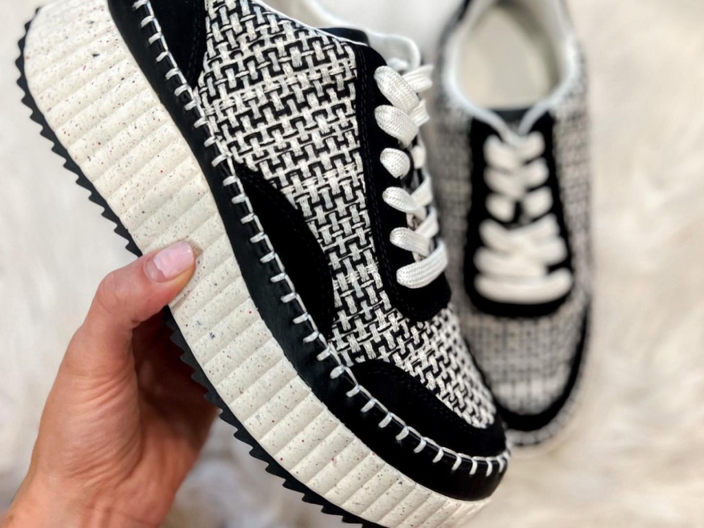 hand holding sneaker with shoe in the background