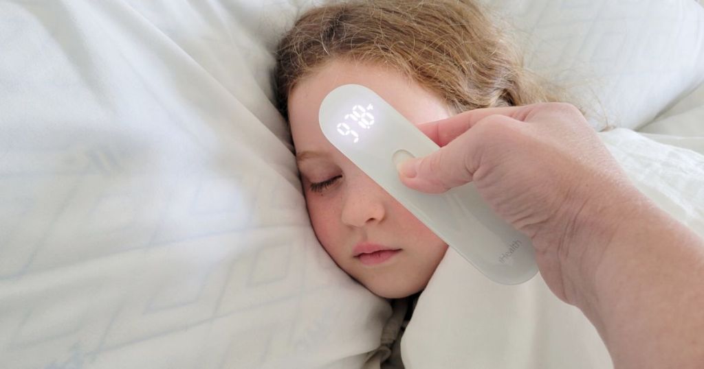 person using no-touch thermometer on girl who is laying in bed