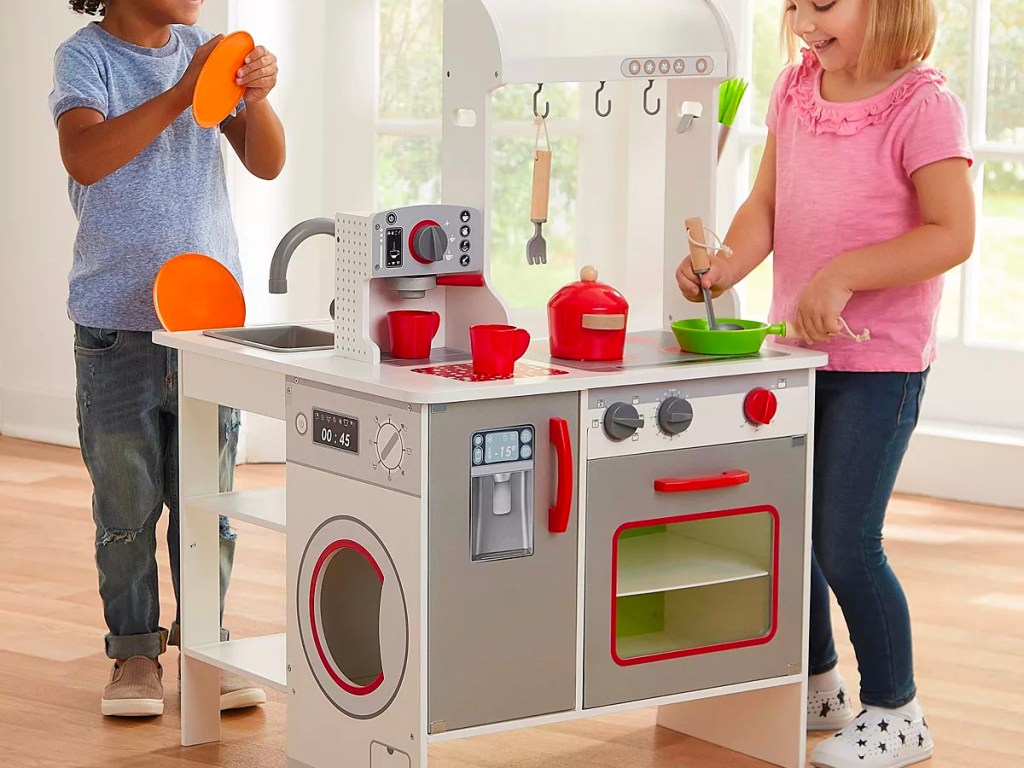 two kids playing with gray and red wooden play kitchen