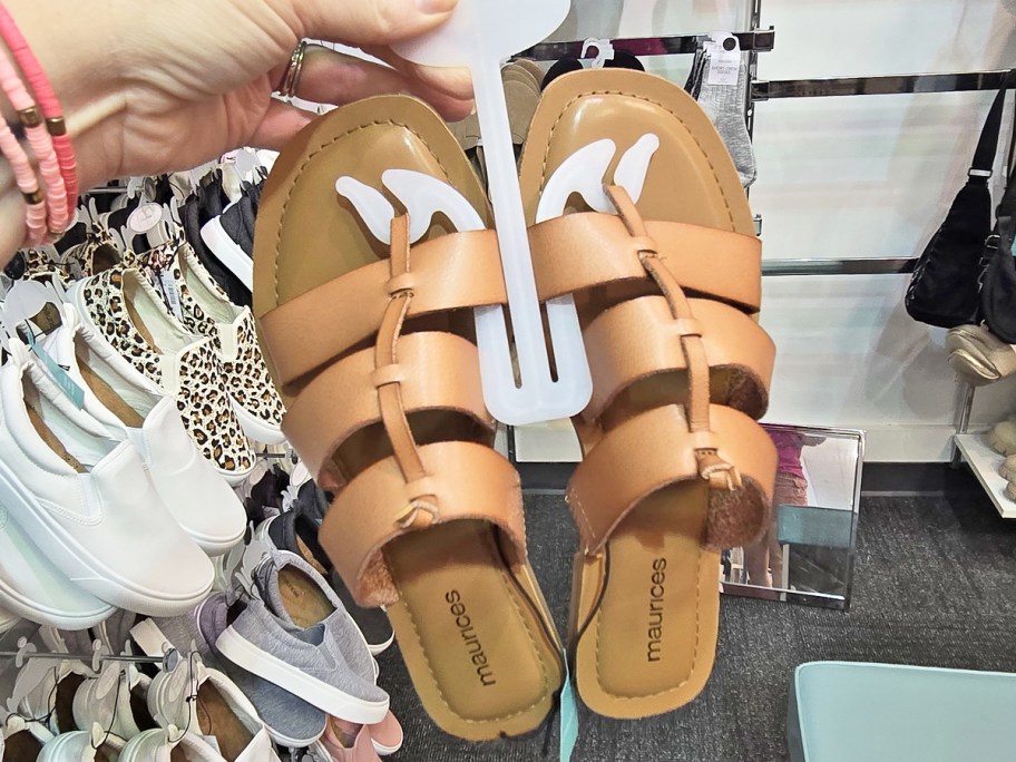 hand holding up a pair of brown leather sandals in store