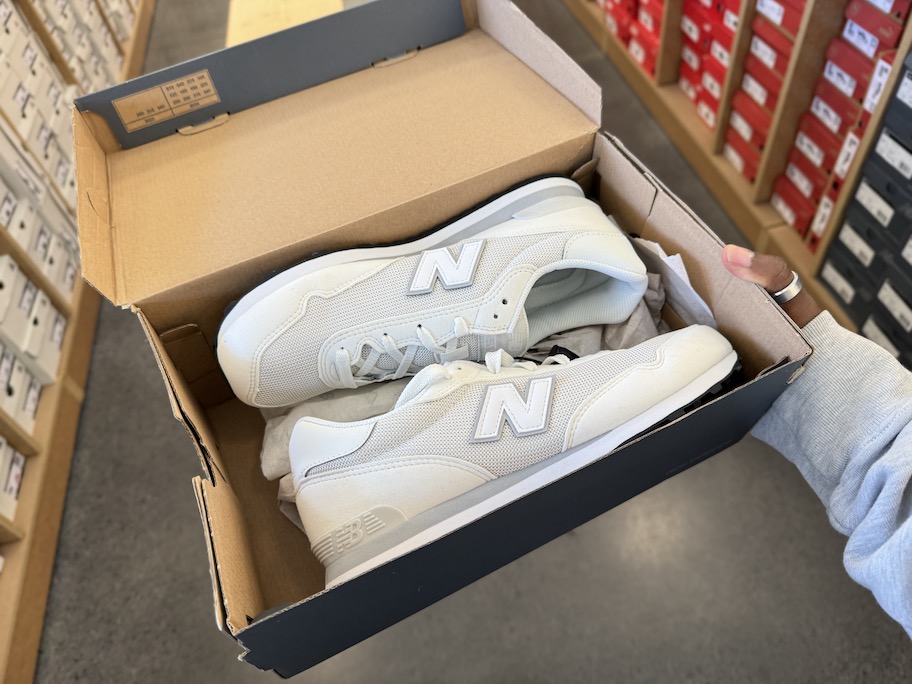 hand holding a new balance shoe box in middle of store aisle