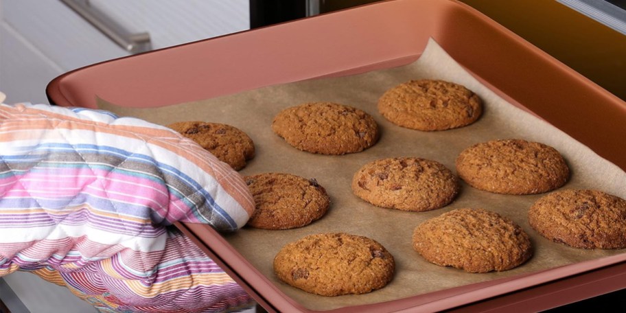 hand putting baking pan with cookies into oven