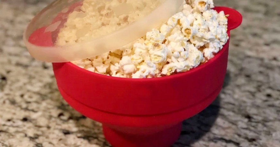 red popcorn bowl full of popcorn with lid laying on top