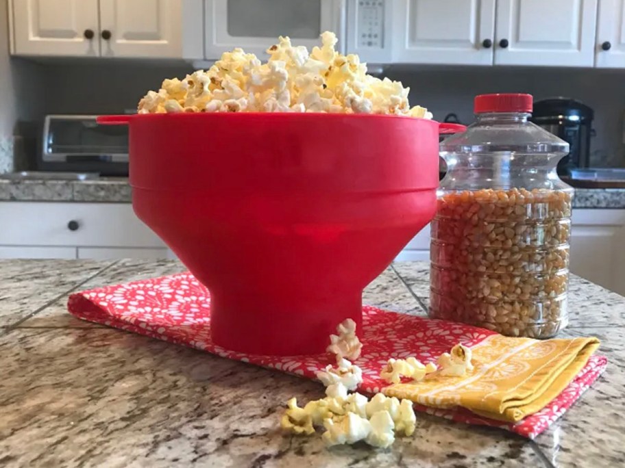 red bowl full of popcorn with container of kernels on countertop