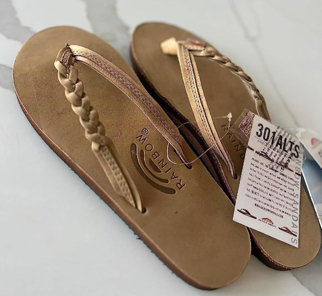 close up of tan colored rainbow flip flops on marble countertop with tags