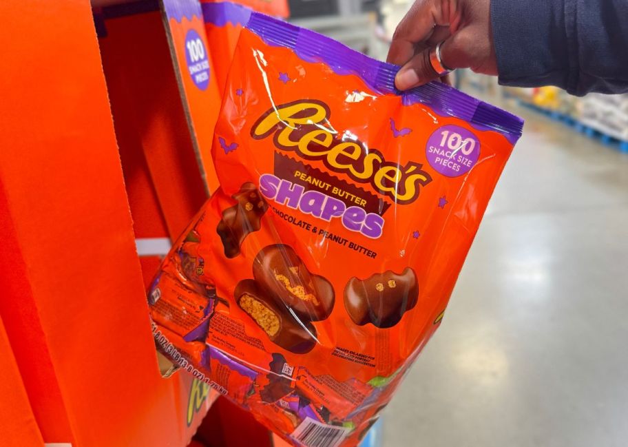 a womans hand grabbing a 100 count bag of reeses shapes