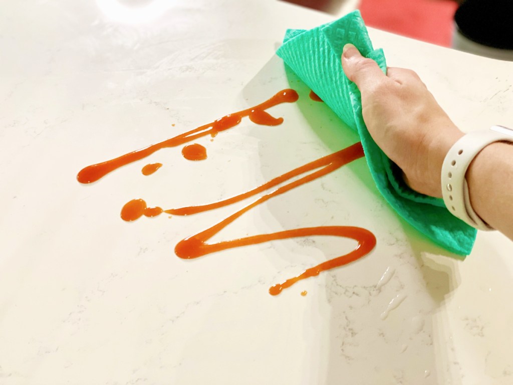 امرأة تستخدم قطعة قماش سويدية لتنظيف الصلصة المسكوبة على سطح عملها