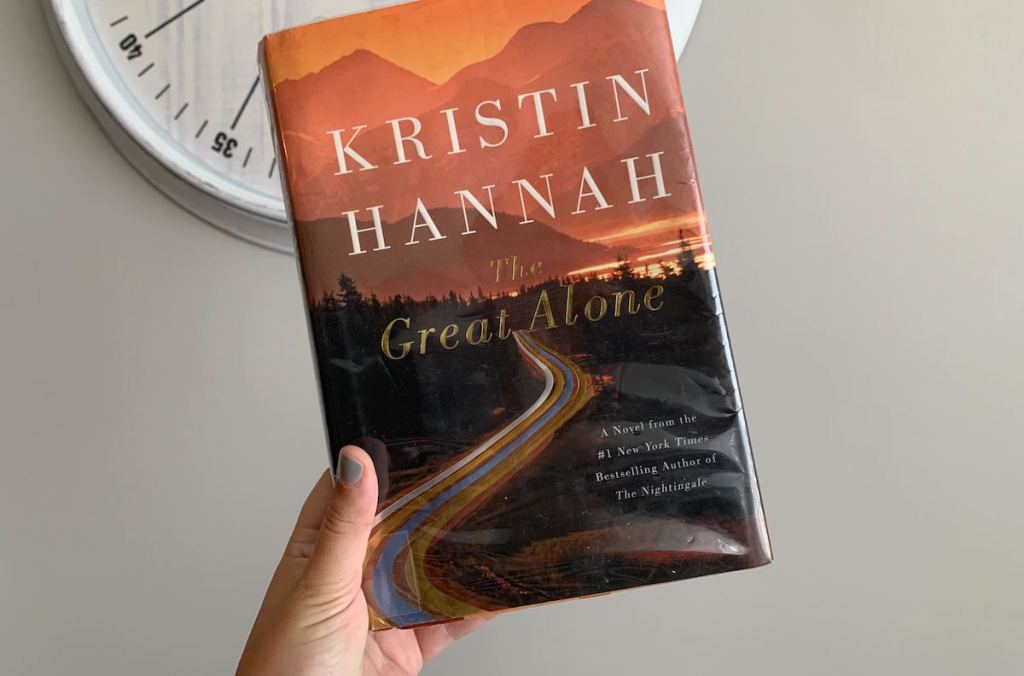 hand holding the great alone book in front of wall clock