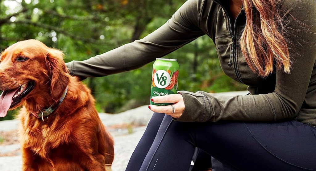 woman hold can of v8 while petting a dog