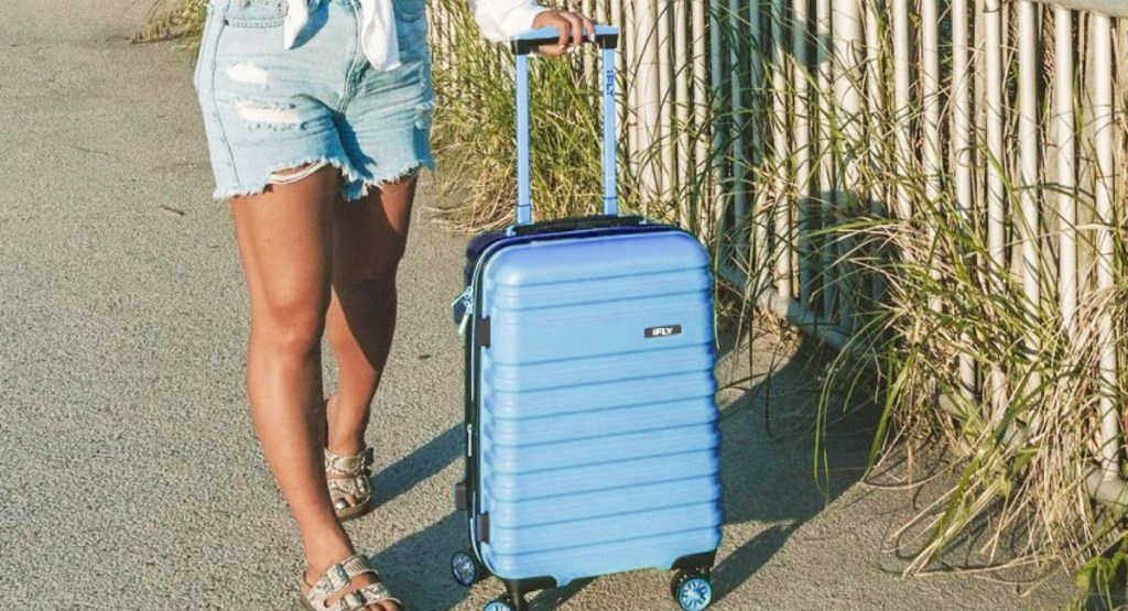 woman holding iFLY luggage at the beach in blue