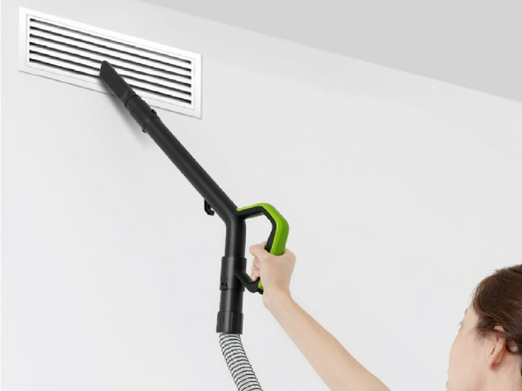 woman vacuuming air vents with vacuum handle