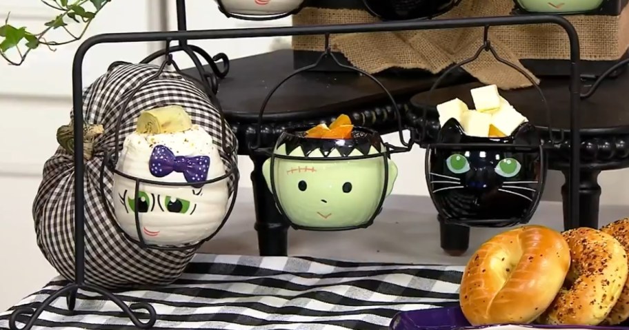 Halloween mummy, Frankenstein and black cat cauldron ramekins hanging from a black wire rack with dip inside