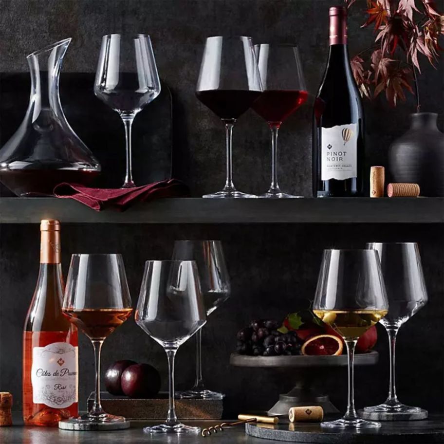 8 stemmed fluted wine glasses with wine in them beside of wine bottles
