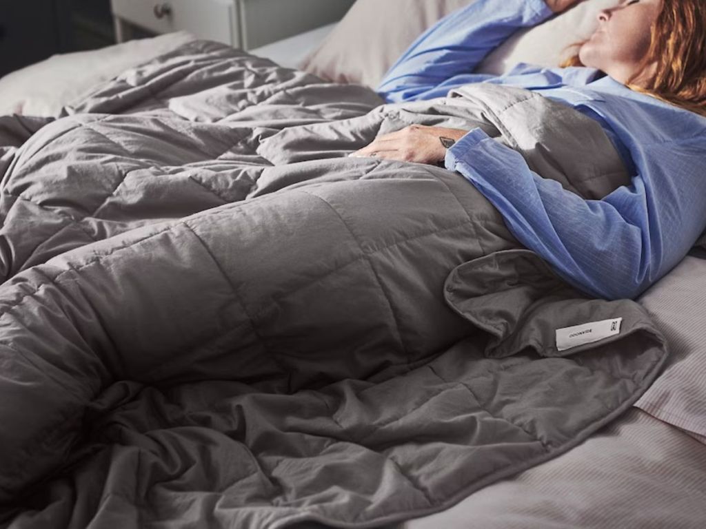 woman laying in bed covered up with a 22lb grey weighted blanket