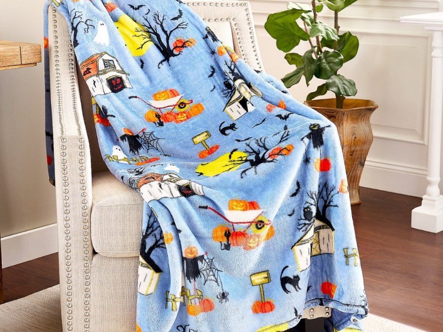 large blue throw blanket with Halloween farm designs over a white accent chair